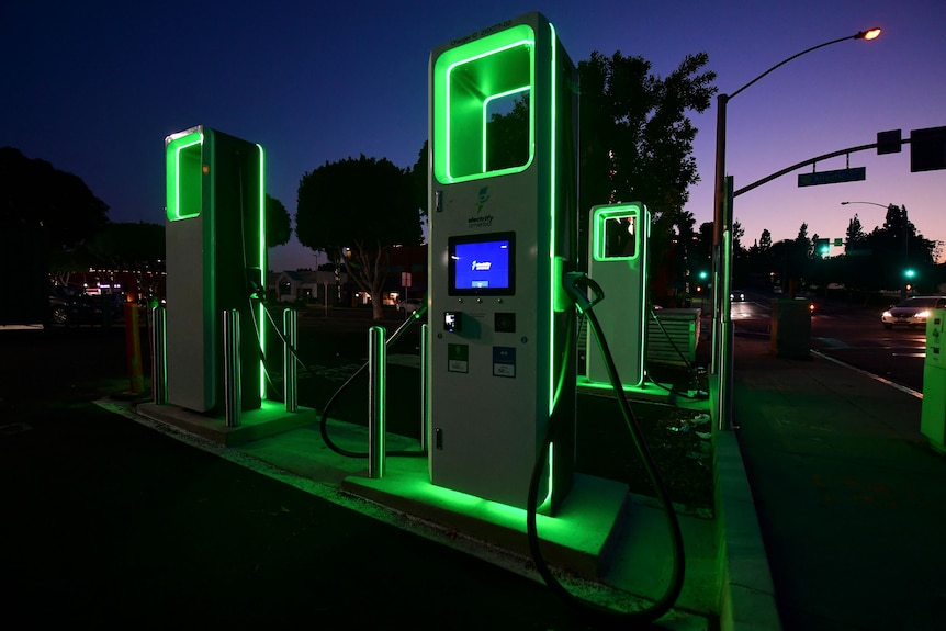 Green-glowing obelisks with charger cables by a roadside at night