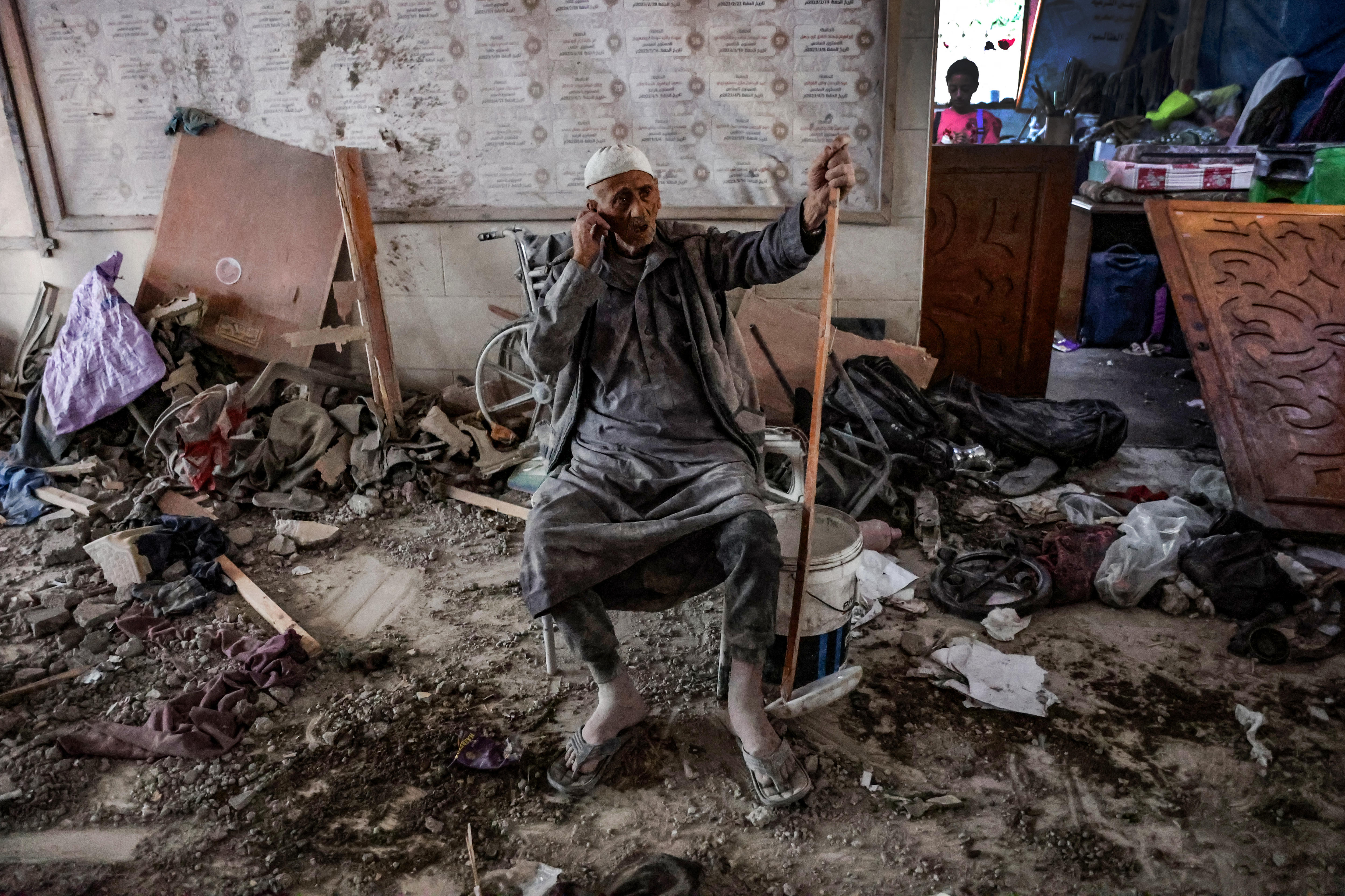 An elderly man sits in a chair amid rubble.