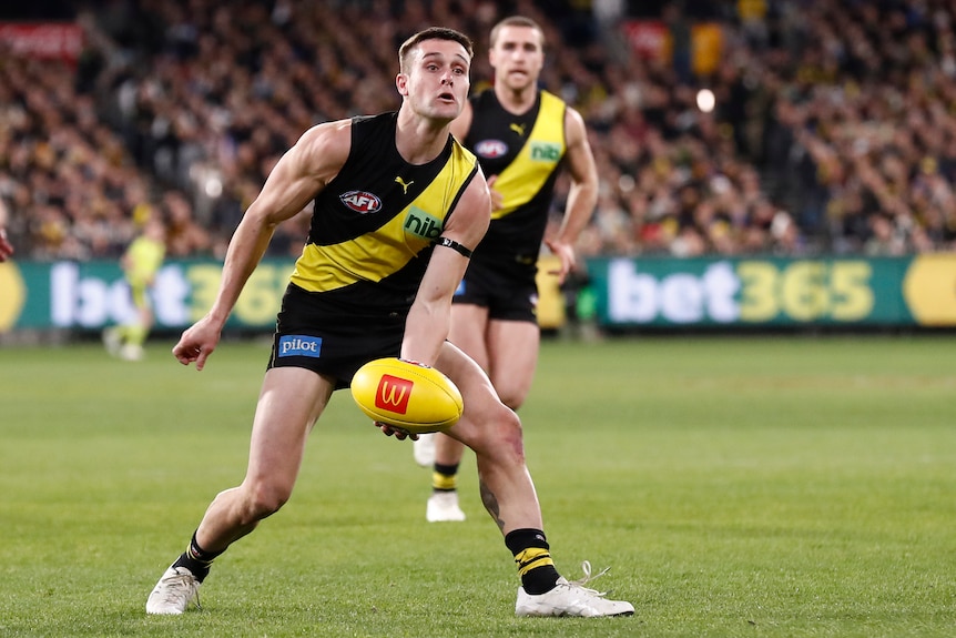 A Richmond player leans to his left as he delivers a handball inboard during a game.