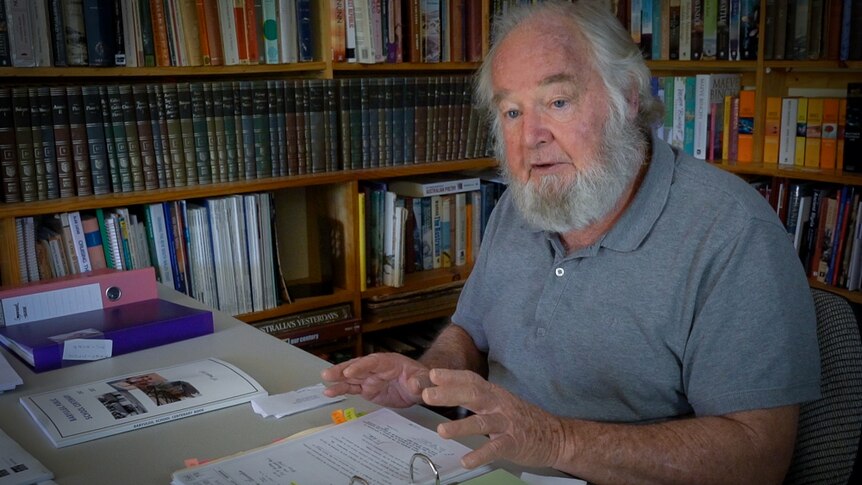 An older man with beard in his home study leafing through a folder of papers.