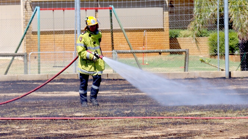 A firefighter hoses down after a blaze at a Kenwick sports oval.