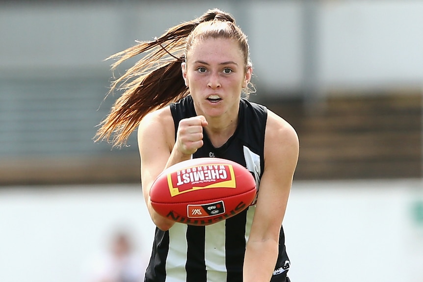 A Collingwood AFLW player handballs during a match against the Bulldogs.