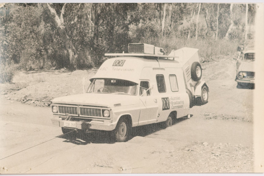 A black and white image of a bogged ABC Darwin broadcast van on a road trip. Scrub is in the background.