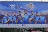 A cyclist rides in front of a large billboard, which has a number of Mumbai Indians players on it