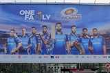A cyclist rides in front of a large billboard, which has a number of Mumbai Indians players on it