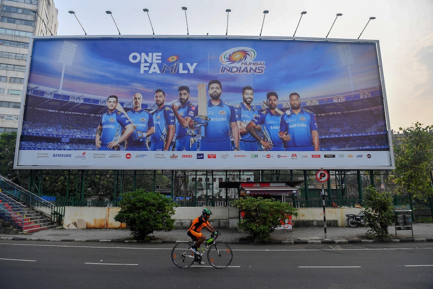 A cyclist rides in front of a large billboard, which has a number of Mumbai Indians players on it