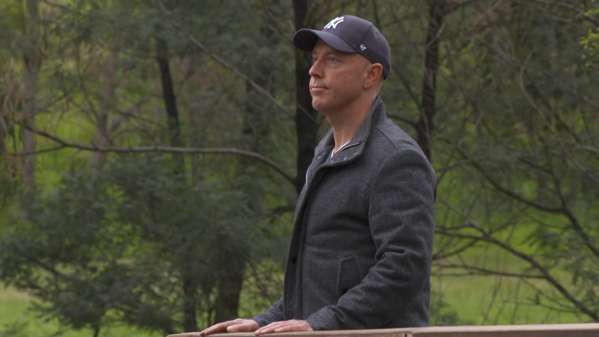 Man wearing a jacket and cap looks out at a park.