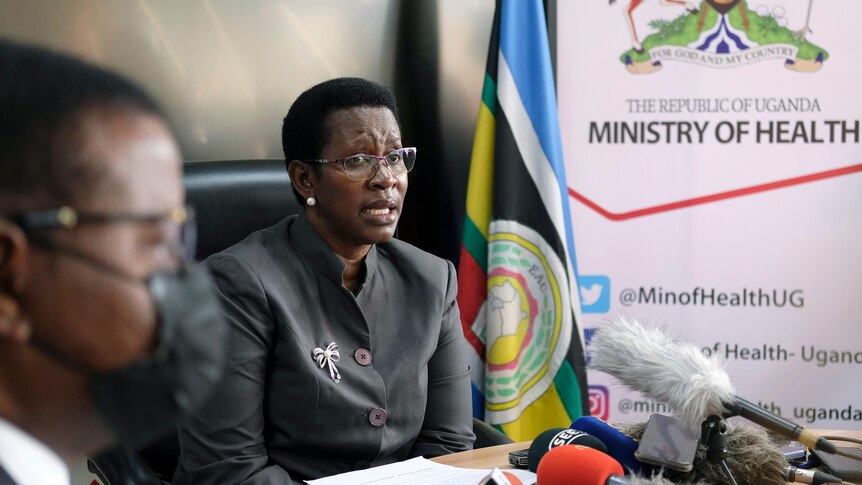 A women in a suit and glasses sits and answers questions during a press conference. 