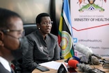 A women in a suit and glasses sits and answers questions during a press conference. 