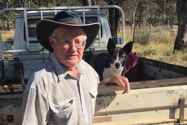 A male grazier smiling with his black and white dog sitting in the back of a ute