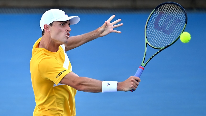 An Australian male tennis player hits a backhand volley.
