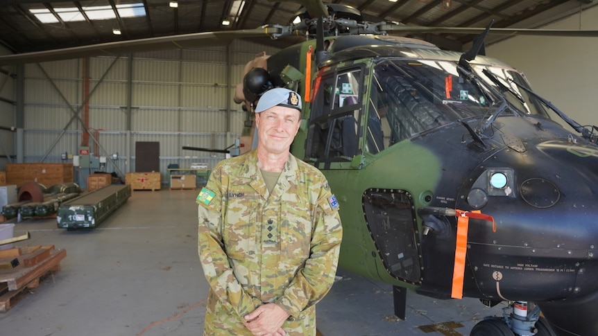A man wearing an Army uniform stands in front of a helicopter.