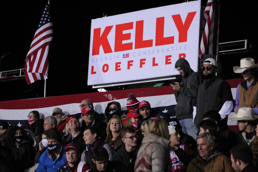 A crowd of people sit in front of a sign saying Kelly Georgia conservative.