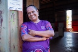 An Indigenous woman leaning up against a door frame with a smile, wearing a pattern t-shirt