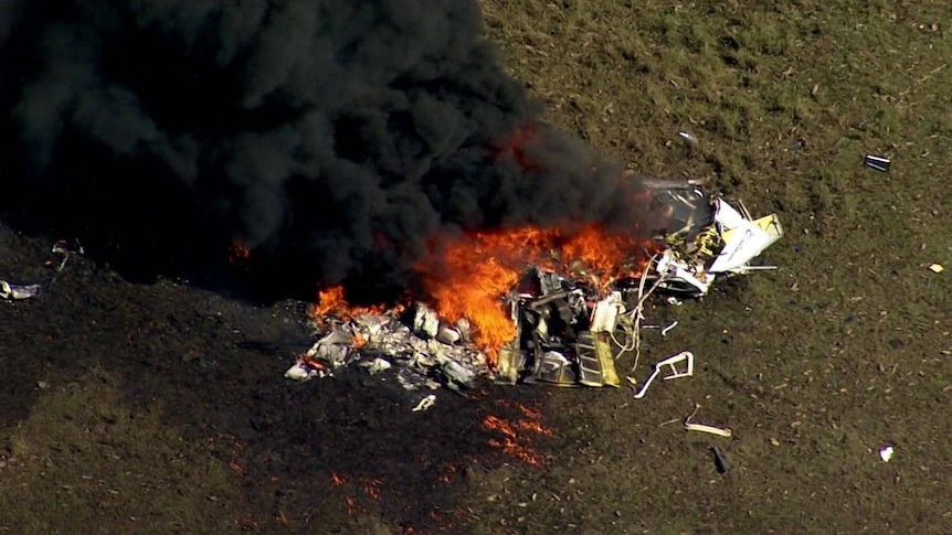 The wreckage of a helicopter with flames and smoke visible