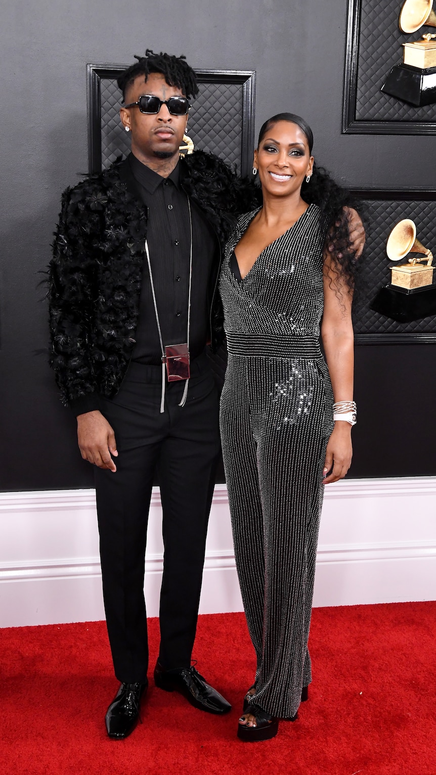 21 Savage wearing a black feathered jacket, standing next to his mother who is wearing a black evening gown