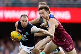 A Carlton AFL player tries to break free of a Brisbane tackle as he holds the ball in one hand.