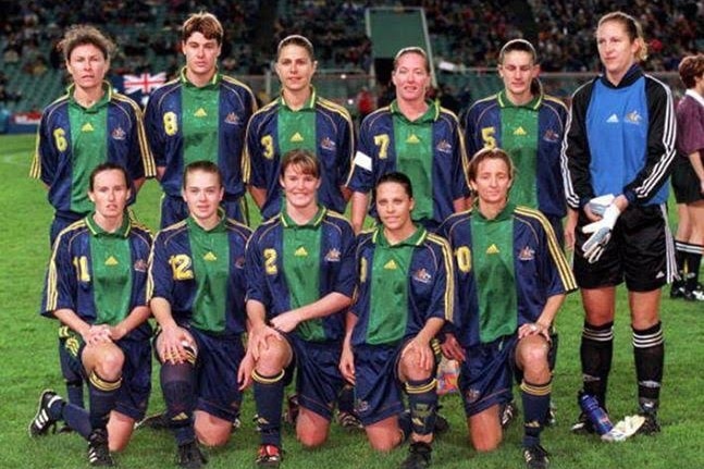 A women's soccer team wearing green, yellow and blue pose for a photo before a game
