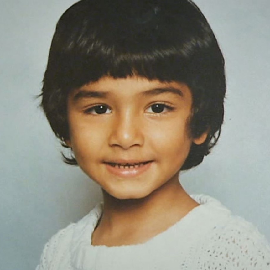 An early 90s headshot photograph of a little boy with dark brown hair, slight smile