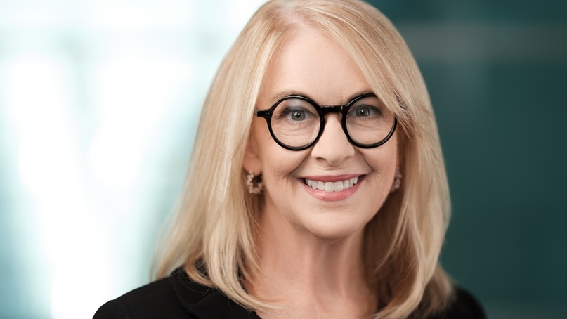A blonde woman smiling with black round glasses. 