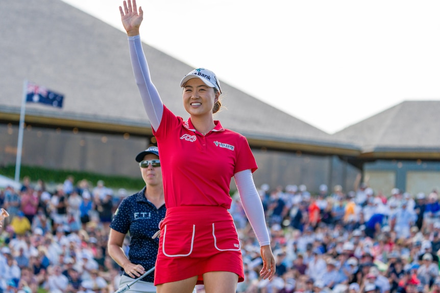 Female golfer in red dress waves to crowd at a golf tournament