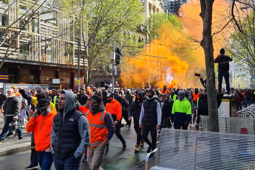 People in hi-vis vests march along Victoria Street, as an orange flare is let off in the background.