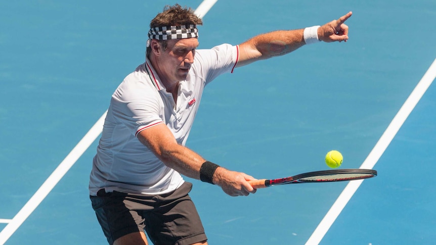 Pat Cash points with one hand while playing tennis on a blue court.