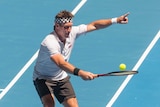 Pat Cash points with one hand while playing tennis on a blue court.