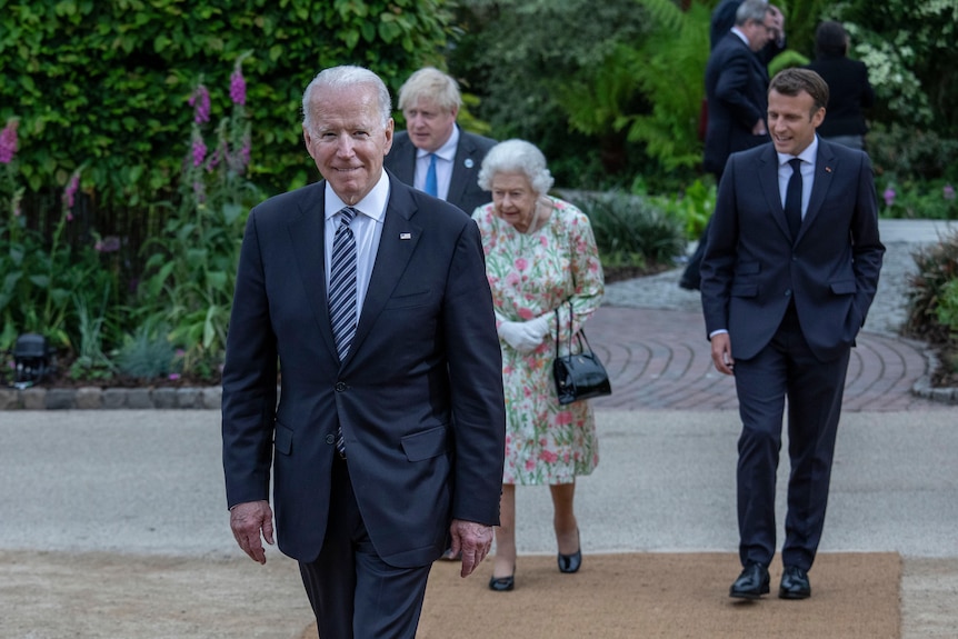 Joe Biden grinning while walking ahead of Emmanual Macron, the Queen and Boris Johnson