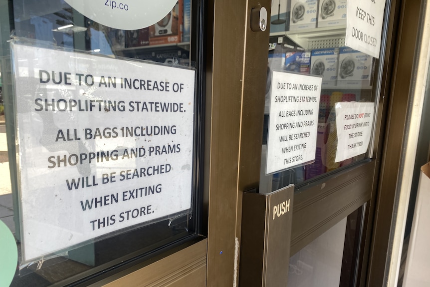 Laminated typed signs about shoplifting on glass doors with metal frames and push handle