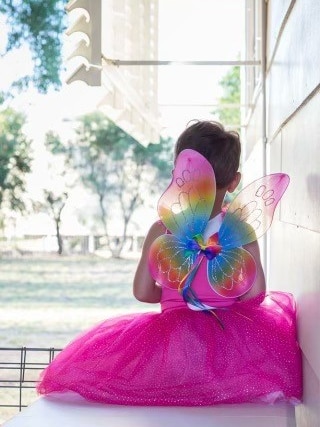 photo taken from behind a young child with short hair sitting on the stairs dresses in a fairy costume