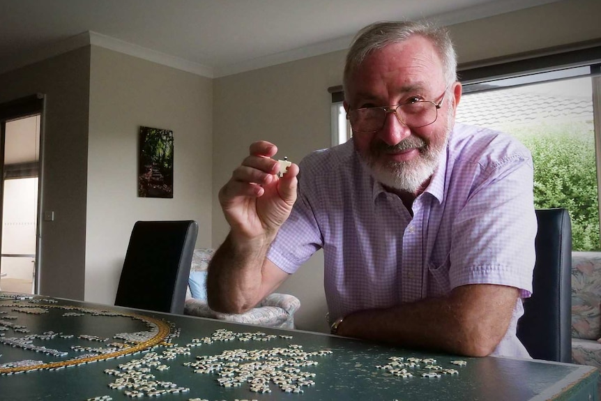 A man holds up a piece of a jigsaw puzzle he is working on.