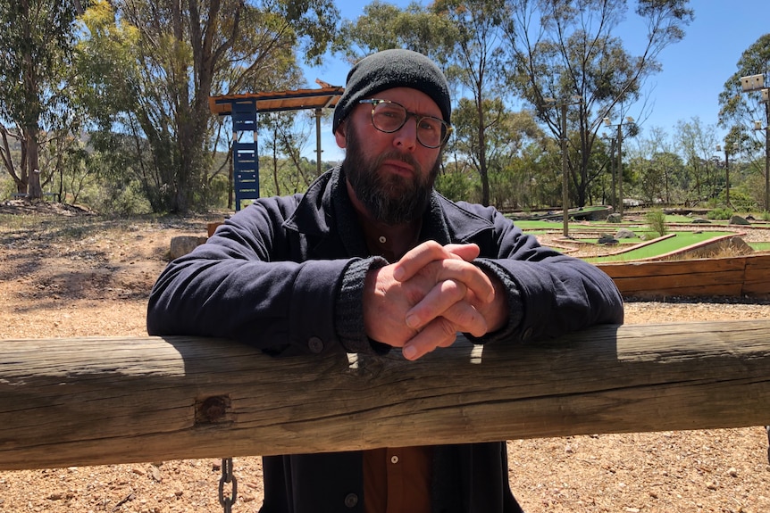 Man leans on a fence railing in a country obstacle course setting.