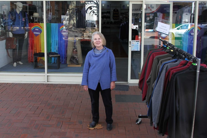 Woman outside of shop with gay pride colours dissplayed.