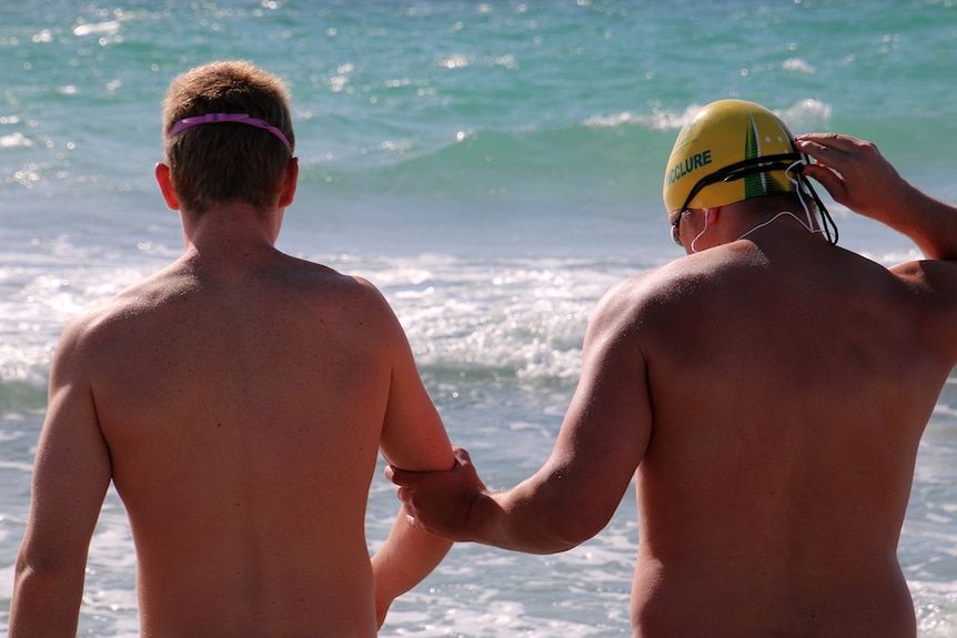 Blind swimmer Jeremy McClure and his guide at the beach, pictured from behind in their swimmers.