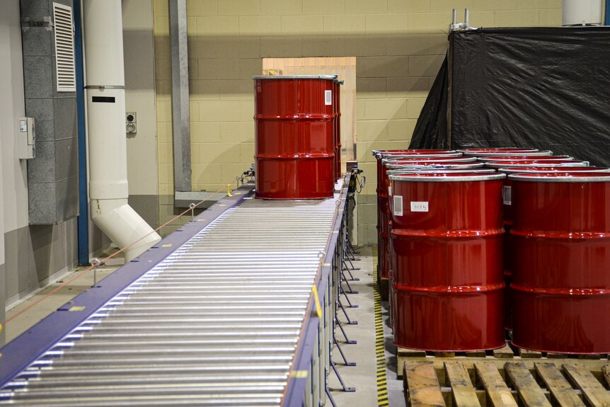The red drums are being lined up on a silver conveyor belt
