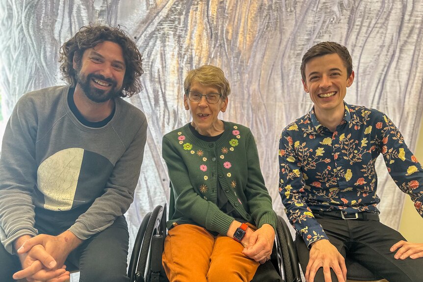 Alon Ilsar, Melinda Smith and Ciaran Frame sit together facing the camera, Melinda is in a wheelchair, they are all smiling.
