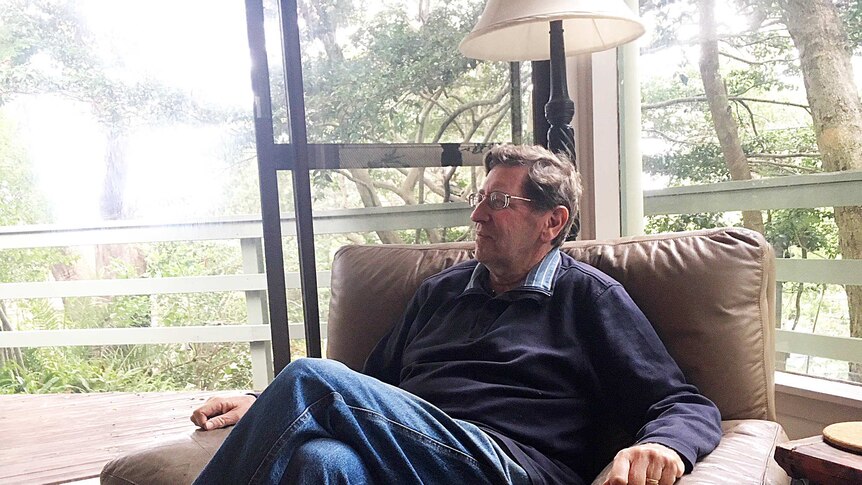 Peter Ricketson sits in a chair in his home, looking out the window.