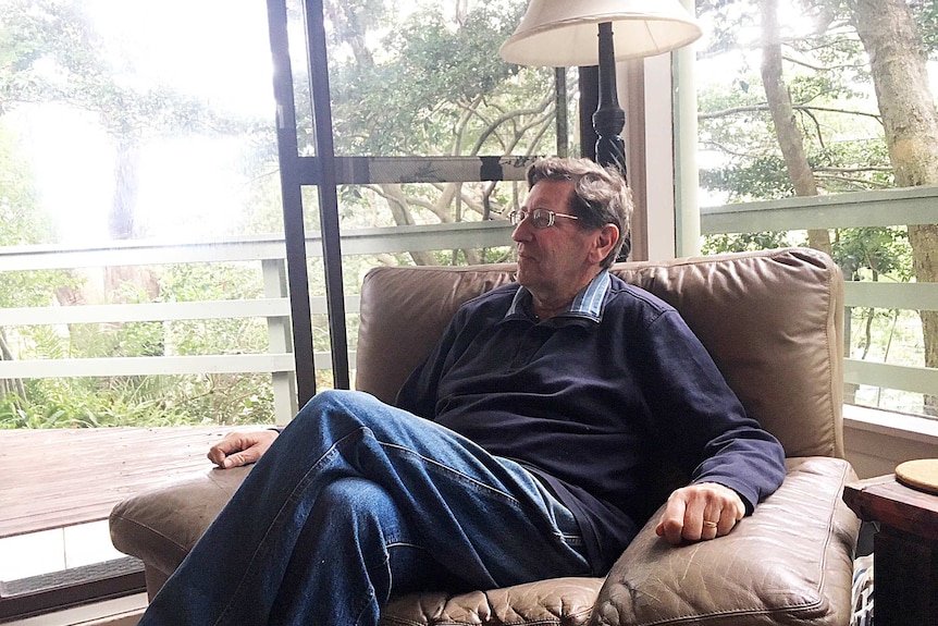 Peter Ricketson sits in a chair in his home, looking out the window.