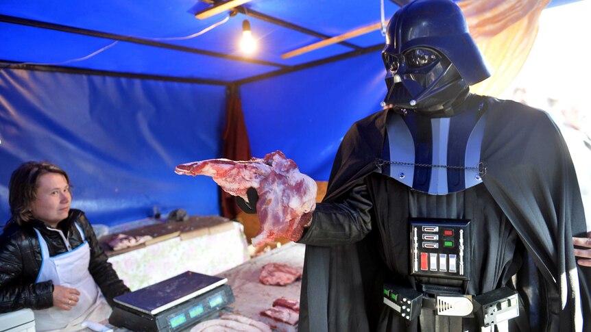 An unnamed protester dressed as Darth Vader grabs a piece of meat from a market stall during a protest.