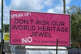 A large pink sign on top of a trailer which reads "Speak up, don't risk our world heritage jewel, vote no to a Daintree bridge"