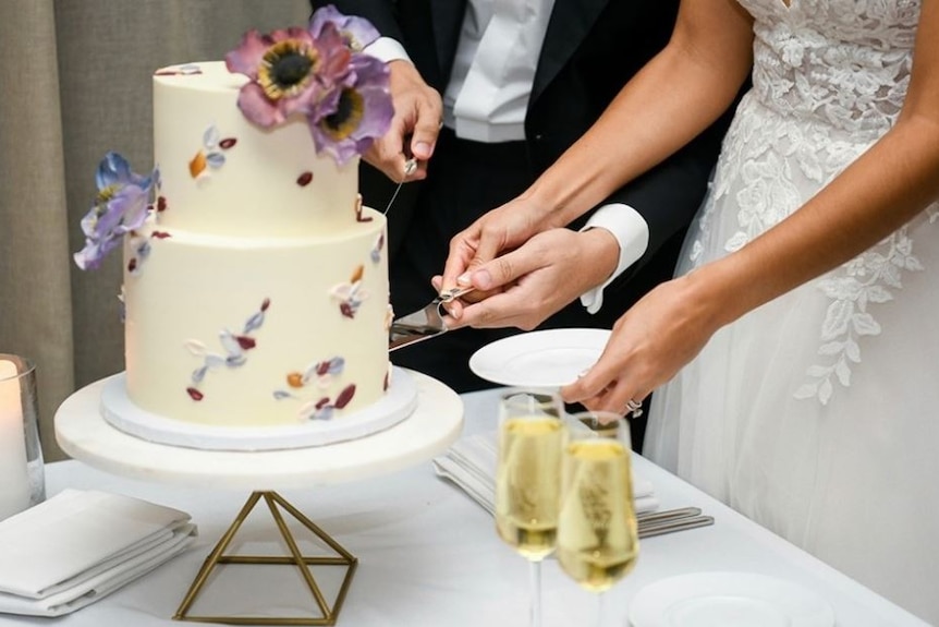 Two people cut a wedding cake with a knife.