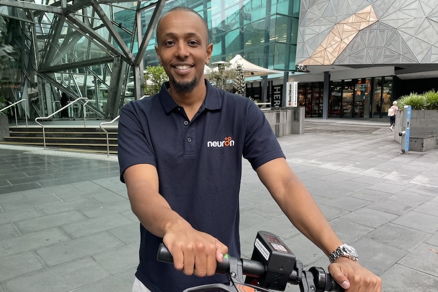 Neuron regional manager Yusuf Abdulahi smiles holding an e-scooter on a street.