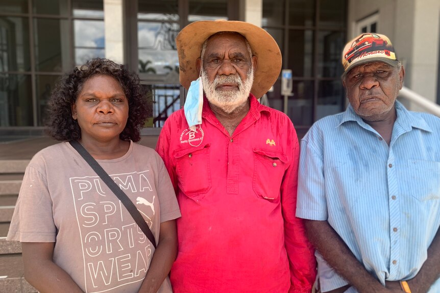Three people with serious expressions stand next to each out outside NT Parliament House.