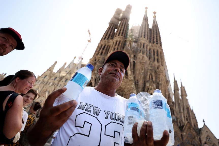A man sells bottles of water for tourists waiting for entrance in the Sagrada Familia basilica in Barcelona,
