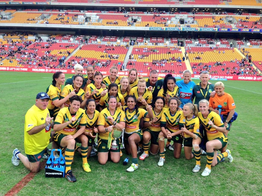The team of Jillaroos huddle together in a stadium, cheering and smiling