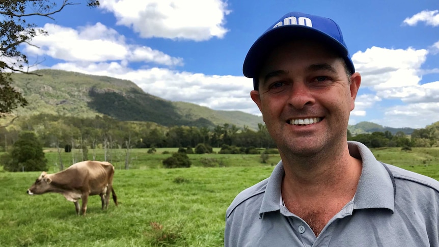 Matthew Trace a dairy farmer standing in a field with a dairy cow behind him.