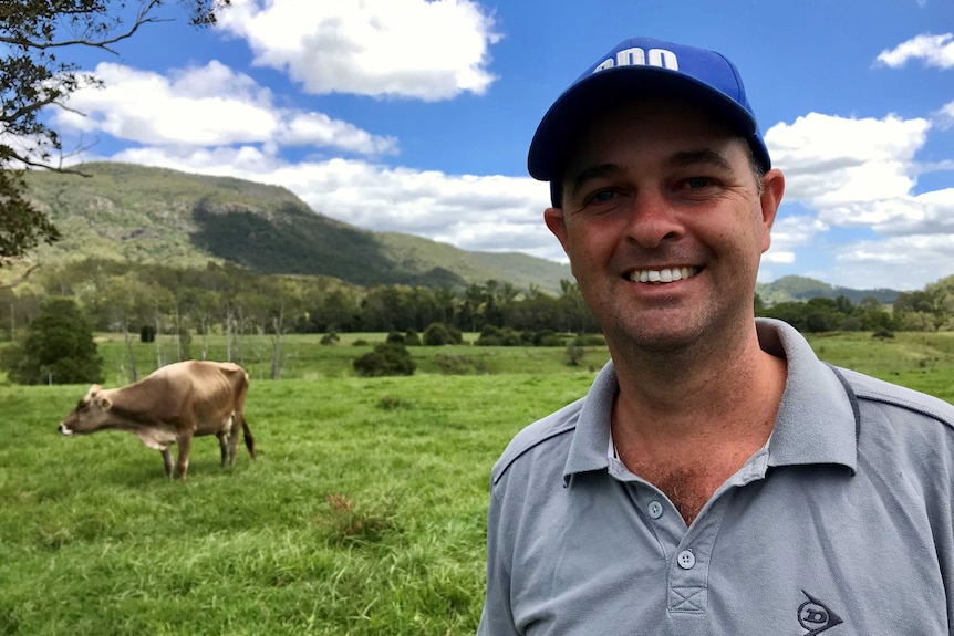 Matthew Trace a dairy farmer standing in a field with a dairy cow behind him.