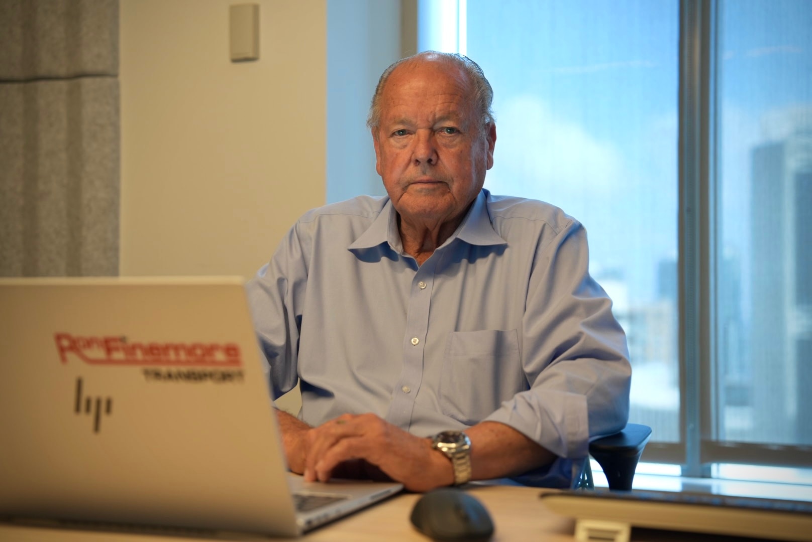 Ron sitting at desk behind a laptop, looking at camera.