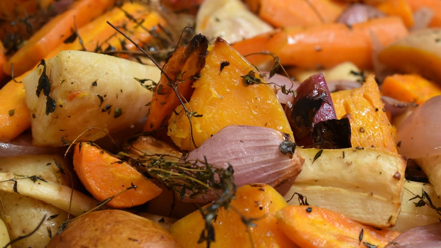 A close-up of roast vegetables including potato, pumpkin, carrot and onion.